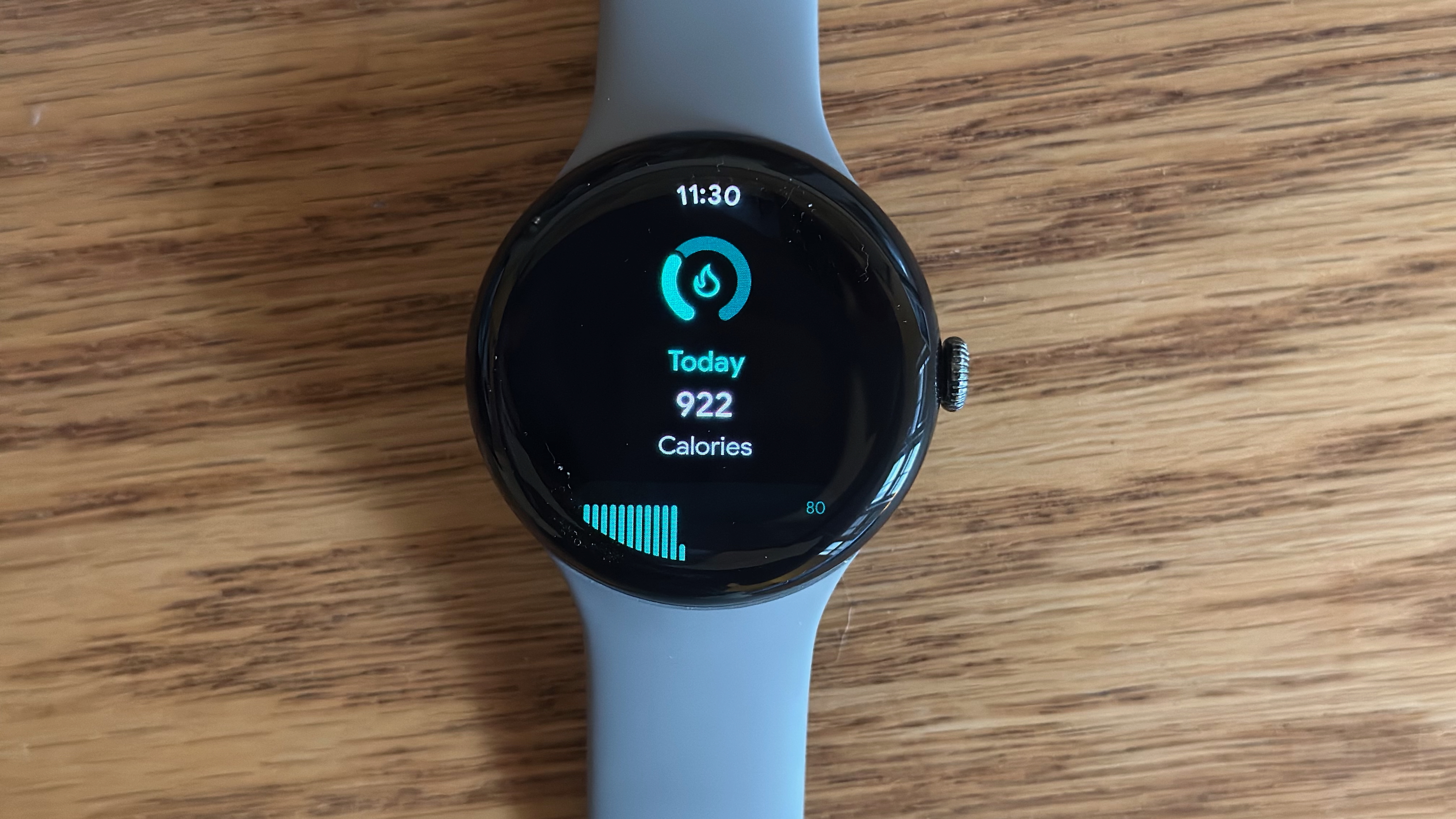 The Google Pixel Watch 3 sitting on a desk, showing a daily calorie count widget.